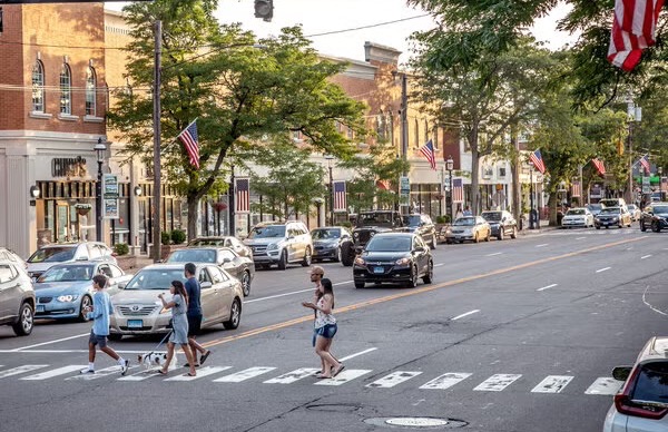 A street crossing near storefronts and cars parked along the curb
